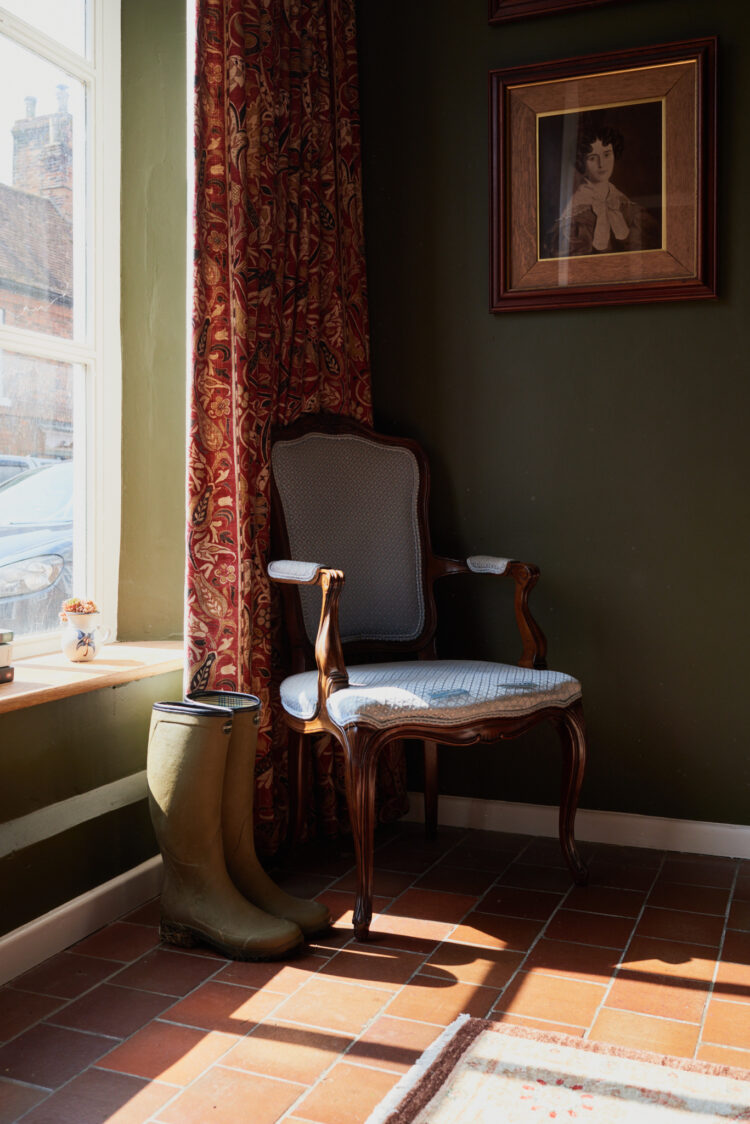 A blue chair with wooden frames in front of a window with a red curtain.